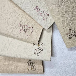 製作をお願いしていた作品が届きました！👍️
青雁皮紙に刺繍。

ねこちゃんと🐈️とウサギさん🐰がとてもキュート！
裏面も和紙を貼ってブックカバーに仕立てました👍️　
カバーはこんにゃく糊を数回塗り紙を強化してありますので長らくお使いいただけます💕

刺繍製作は@omamagotolavo_art　さん
ありがとうございました☺

The piece I commissioned has finally arrived! 👍️✨

Embroidered on blue gampi paper.

The little cat 🐈️ and bunny 🐰 are absolutely adorable! 💕
The back is also covered with washi paper and finished as a beautiful book cover. 👍️

The cover has been strengthened by applying several layers of konnyaku paste, making it durable enough to be enjoyed for a long time. 💕

#和紙に刺繍
#ブックカバー
#和紙のステーショナリー
#県立博物館おきみゅー
#浦添市美術館
